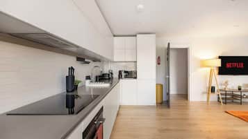 A modern kitchen with white cabinetry, a black countertop, and a built-in oven. There is a microwave, kettle, and coffee maker on the counter. A fire extinguisher is mounted on the wall.