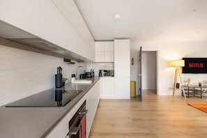 A modern kitchen with white cabinetry, a black countertop, and a built-in oven. There is a microwave, kettle, and coffee maker on the counter. A fire extinguisher is mounted on the wall. - 3BR Wembley Stadium Retreat 1 min Walk to Station (Wembley Park)