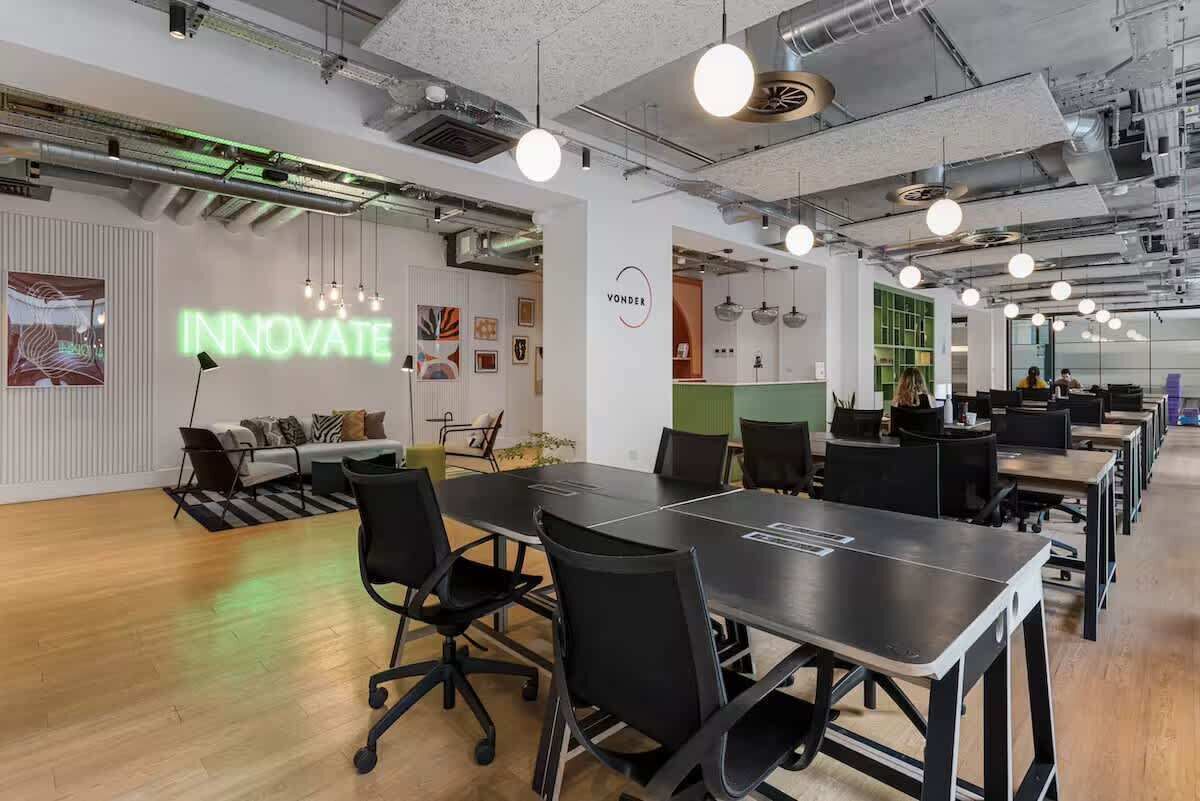 An office space with a large conference table, black office chairs, and a 'VONDER INNOVATE' sign on the wall.