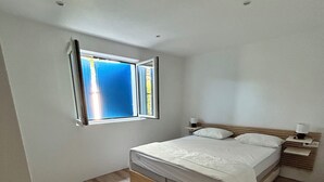 Quarto com uma cama de solteiro, mesa de cabeceira, janela e piso de madeira.