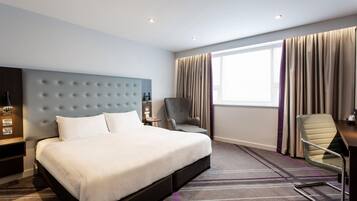 A hotel room with a large bed, a desk, a chair, a nightstand, and a window with curtains.