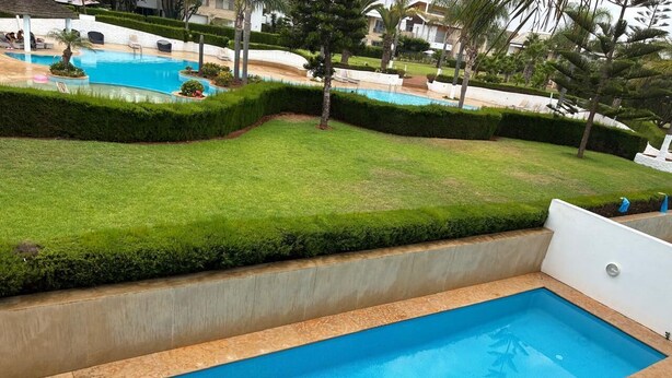 Una piscina rectangular con interior azul, rodeada por un bajo muro de concreto y un césped con setos bien recortados.