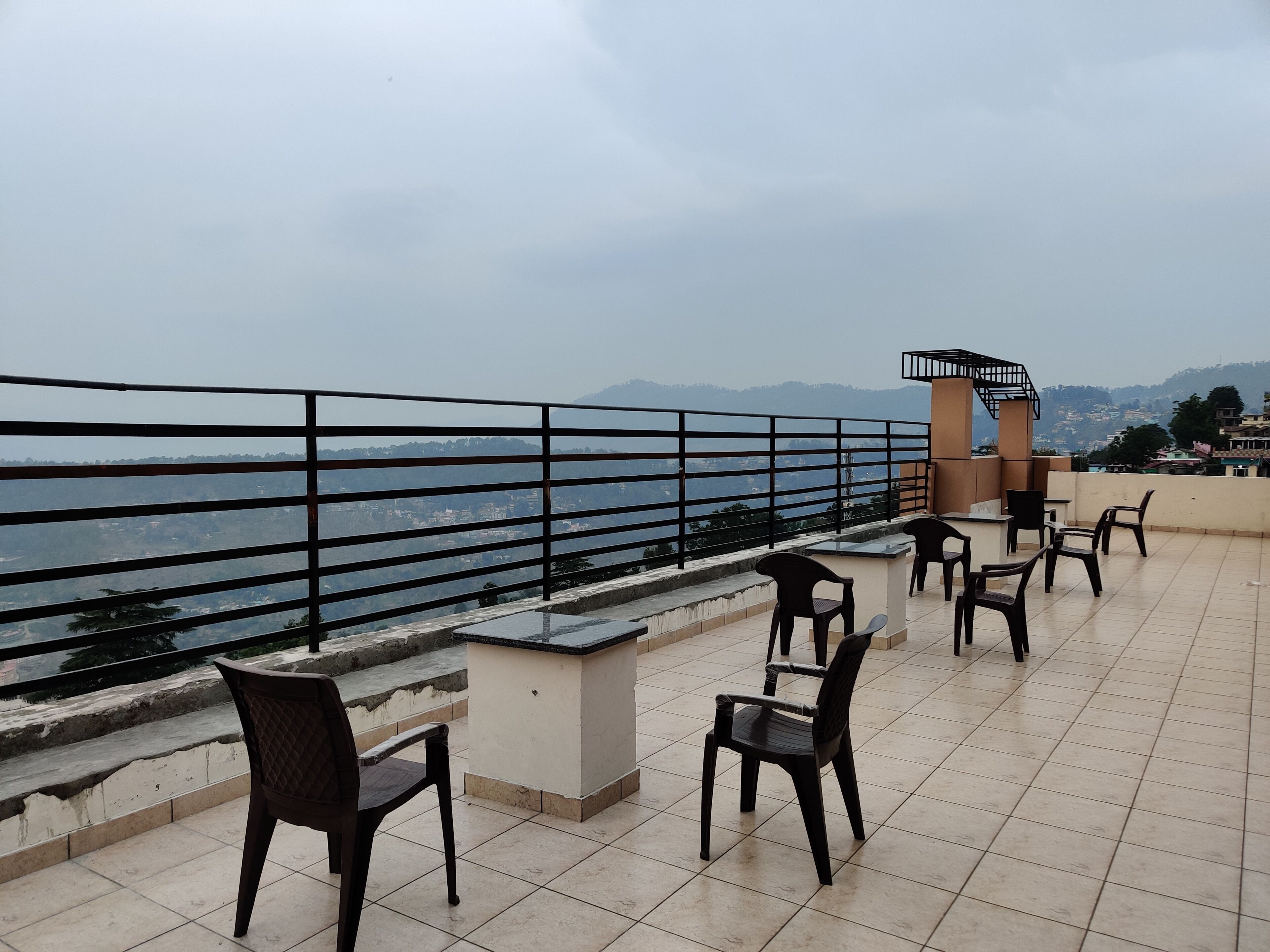 A terrace with chairs and a table, overlooking a body of water and distant hills.