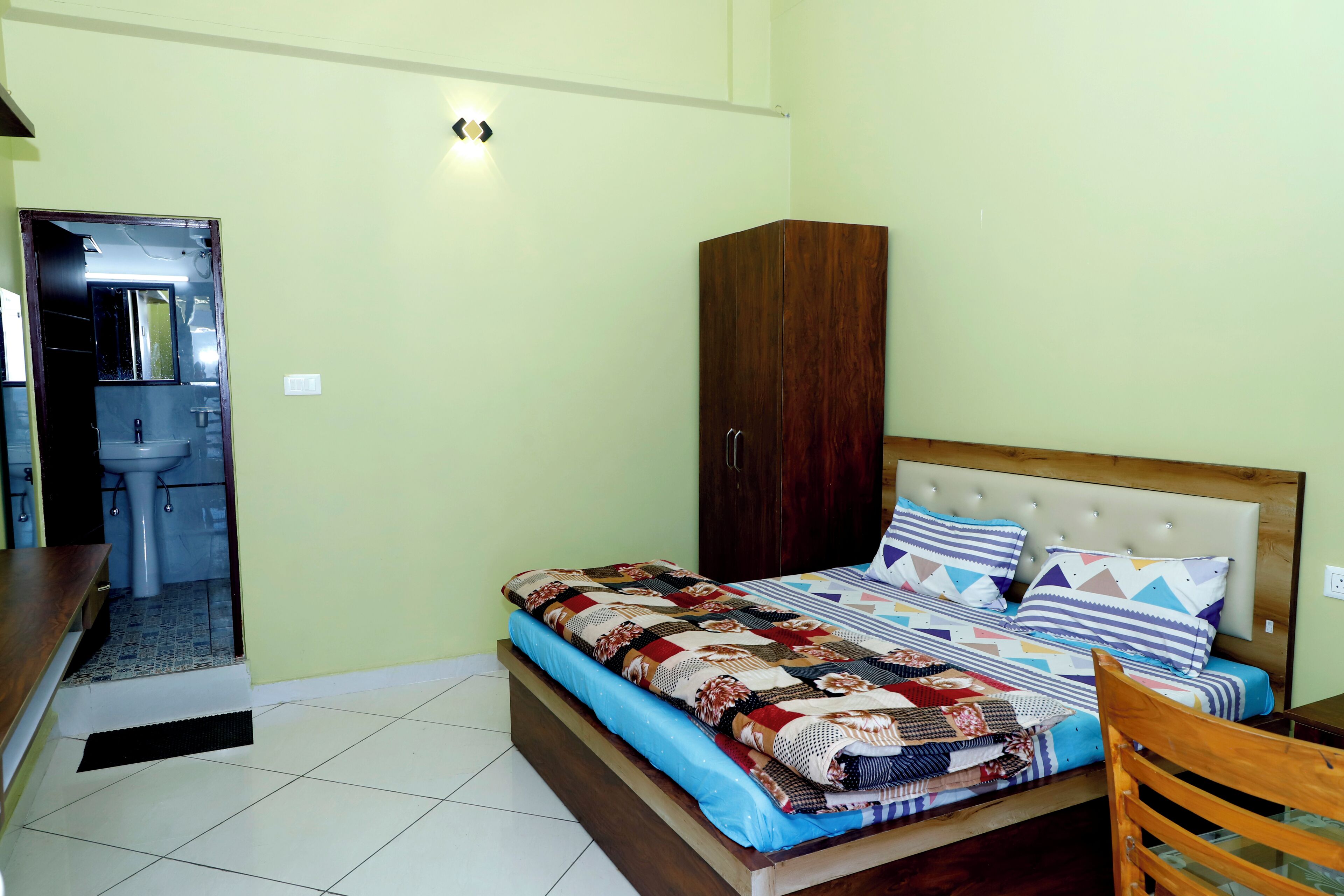 A bedroom with a bed, a wooden wardrobe, a bathroom with a sink, and a mirror.