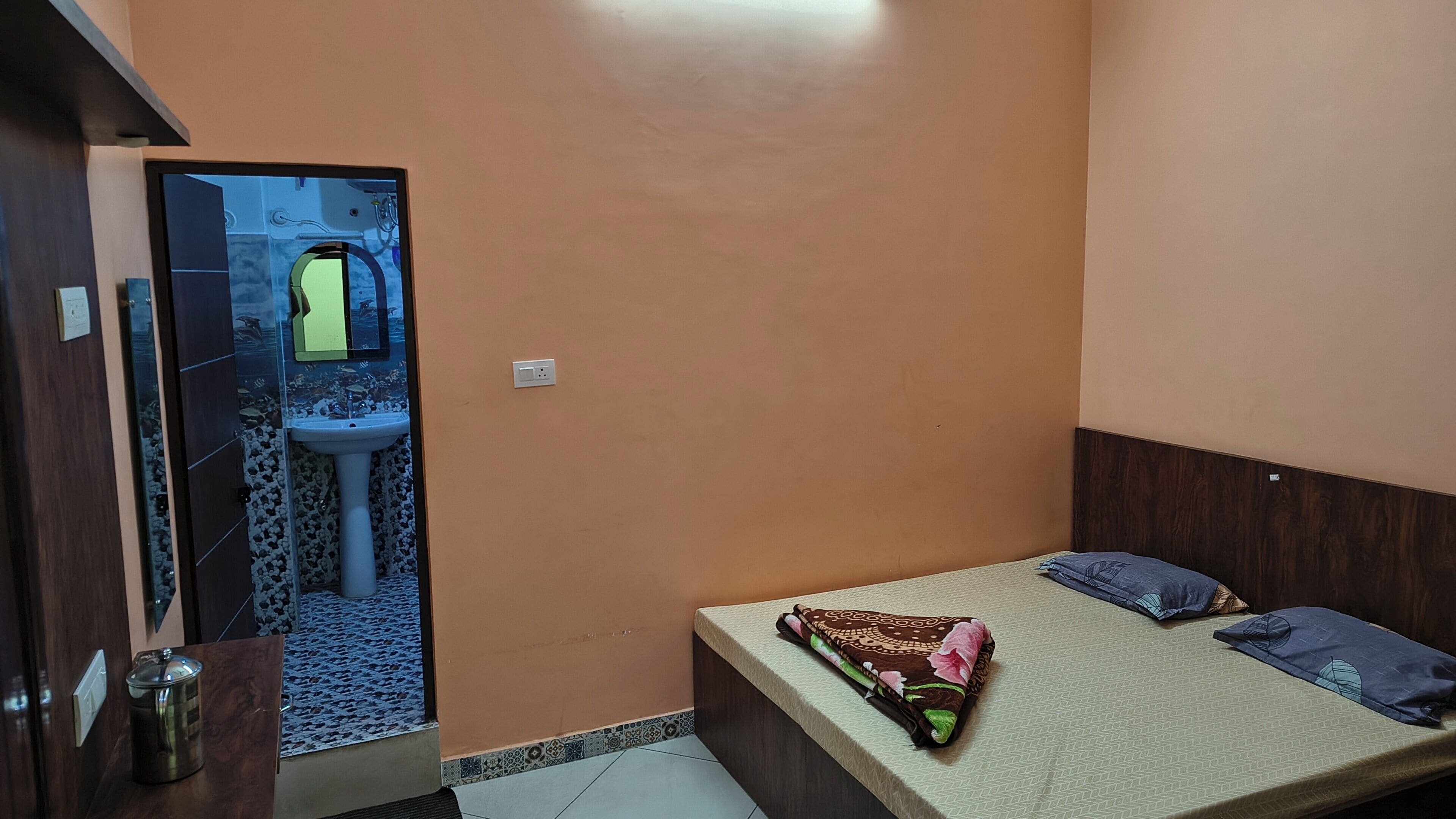A small, compact room with a bed, a bedside table, a sink, and a mirror.