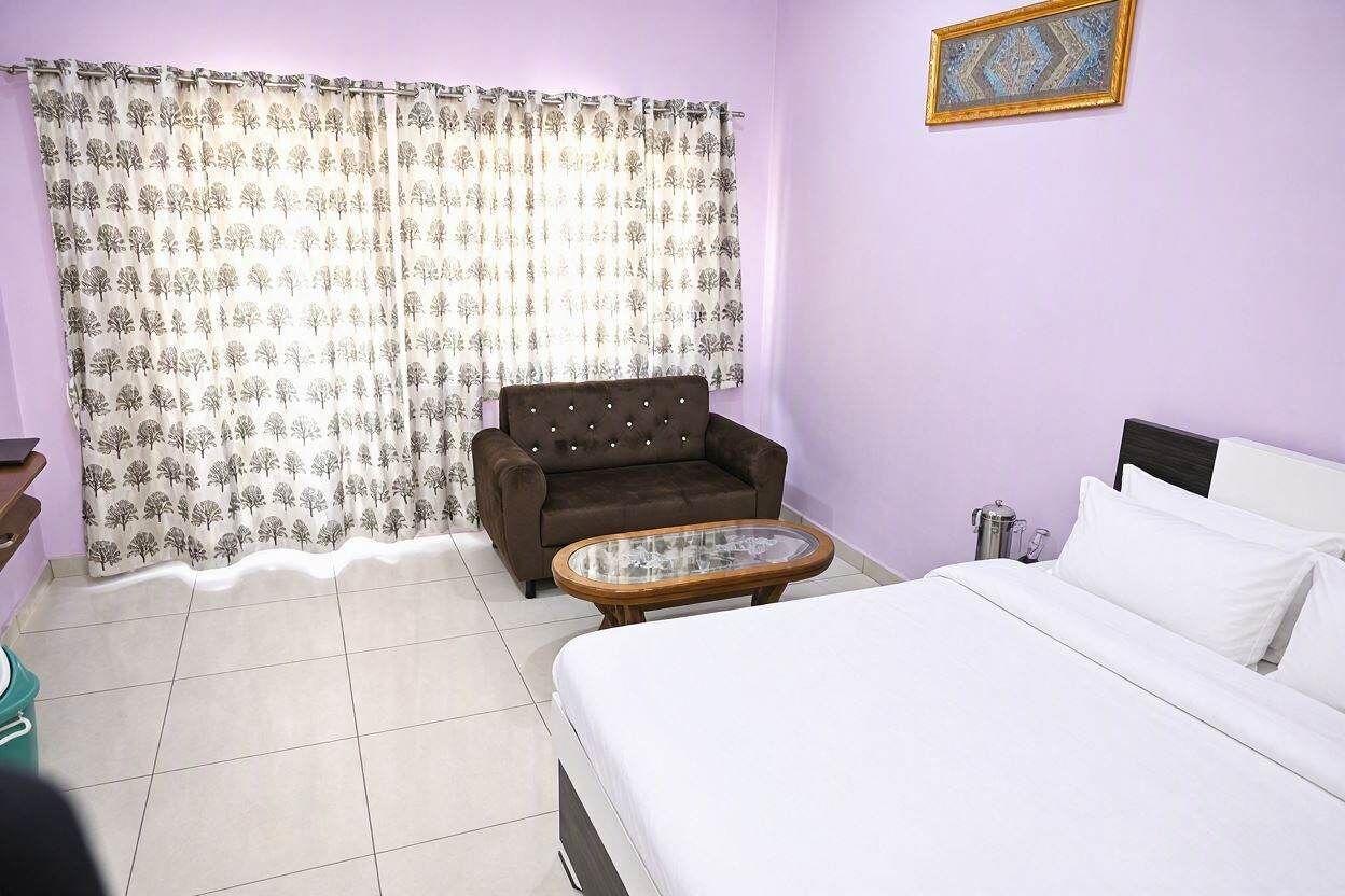 Una habitación con cama, sofá, una mesita y cortina con estampado de árbol.