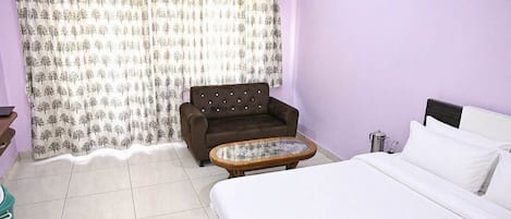 Una habitación con cama, sofá, una mesita y cortina con estampado de árbol.