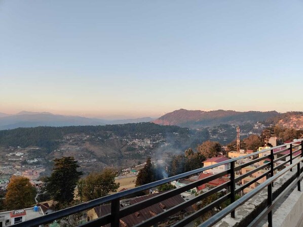 A panoramic view of a mountainous landscape with a town below, a clear sky, and a distant mountain range. - HOTEL ALMORA INN (Almora)