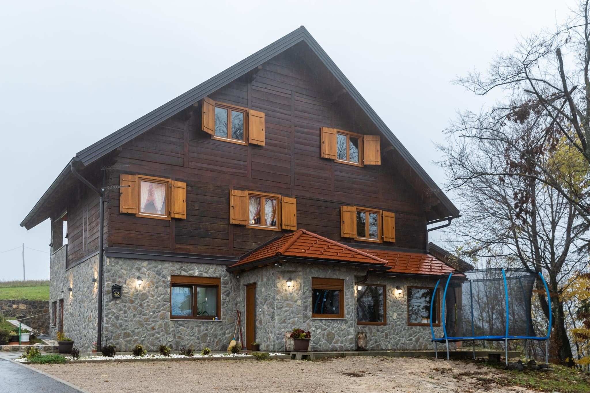 Ein zweistöckiges Holzhaus mit Steinunterbau, mehreren Fenstern mit Fensterläden und einer kleinen Veranda.