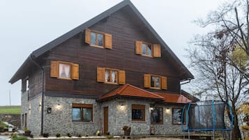 Ein zweistöckiges Holzhaus mit Steinunterbau, mehreren Fenstern mit Fensterläden und einer kleinen Veranda.