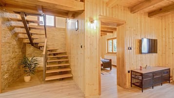 A wooden interior with a staircase, a bed, a TV, and a plant.