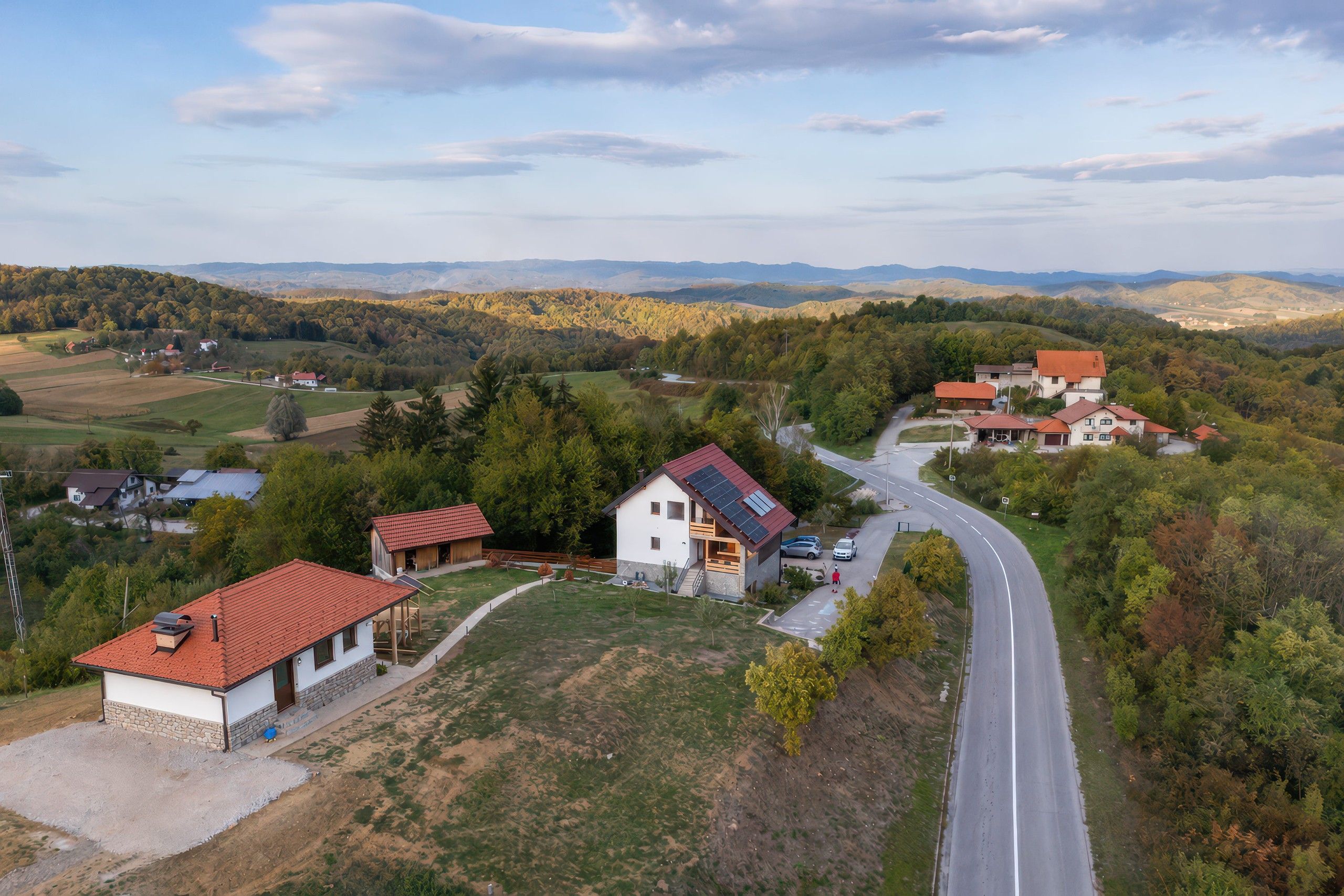 A rural landscape with a winding road, houses, and a valley.