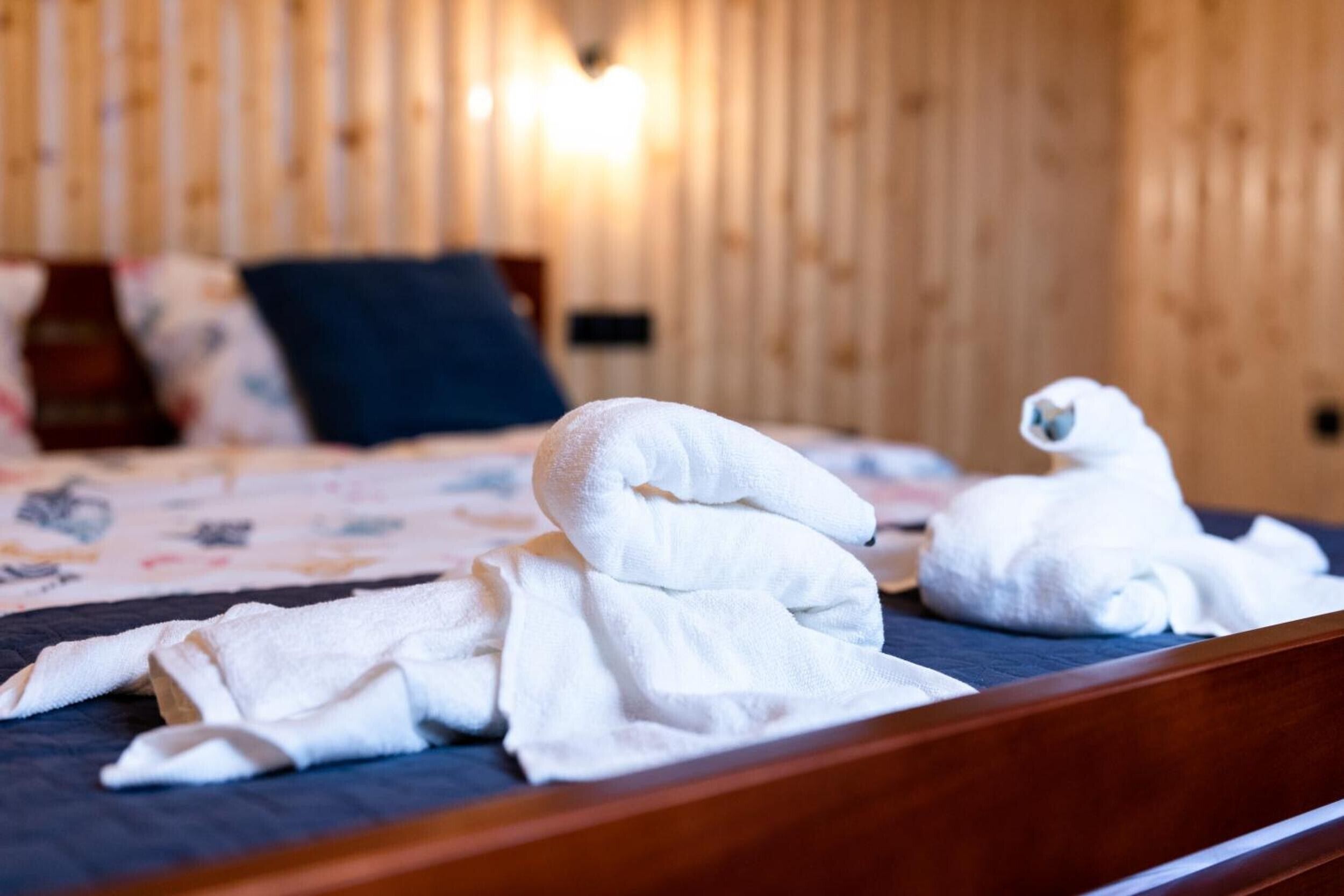 Una camera d'albergo con una parete in legno, un letto con copriletto blu e due asciugamani piegati sul letto.