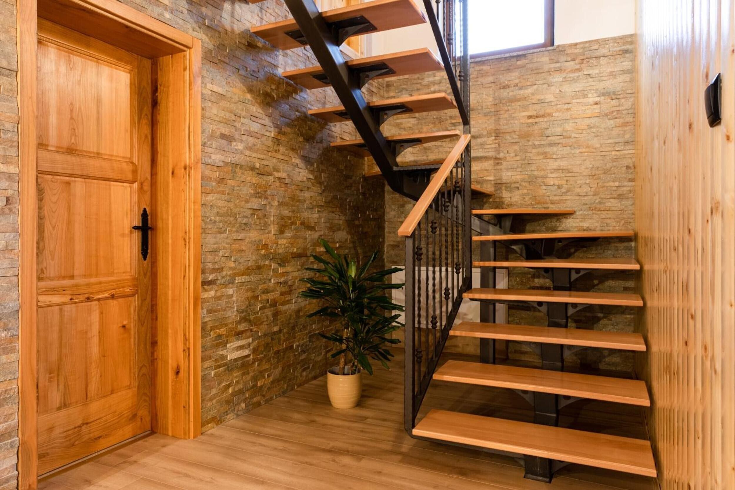 A wooden staircase with a metal railing, a wooden door, and a potted plant.