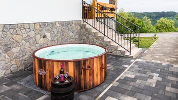 A spa area with a wooden hot tub, a stone wall, and a staircase leading to a deck.