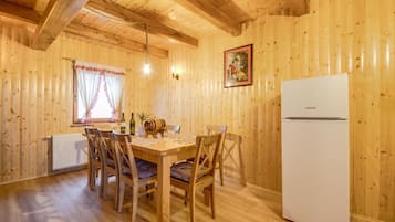Ein Holzinnenraum mit Esstisch, Stühlen, einem Kühlschrank und einem Fenster mit Vorhängen.