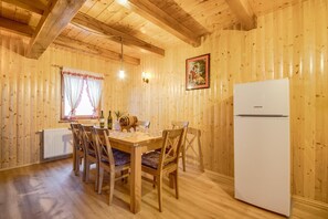Ein Holzinnenraum mit Esstisch, Stühlen, einem Kühlschrank und einem Fenster mit Vorhängen.