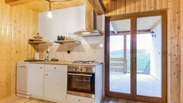 Un intérieur en bois comprenant un espace cuisine, avec un poêle, un four et des placards.