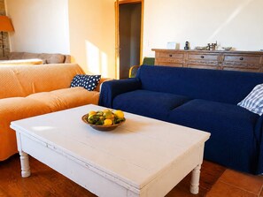 A living room with two sofas, one orange and one blue, a white coffee table with a bowl of fruit, and a wooden cabinet with decorative items. - Stone House Central Filiatra - 7min from the Beach (Filiatra)