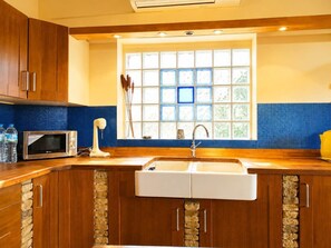 A kitchen with wooden cabinets, a microwave, a sink, and a window with blue-tiled walls. - Stone House Central Filiatra - 7min from the Beach (Filiatra)