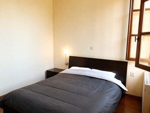 A single bed with a dark headboard, a bedside table, a wall-mounted light, and a window with a wooden frame. - Stone House Central Filiatra - 7min from the Beach (Filiatra)