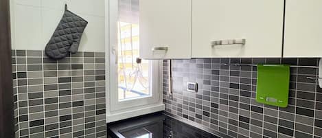 A compact kitchen with white cabinets, a black countertop, and a window with a view.