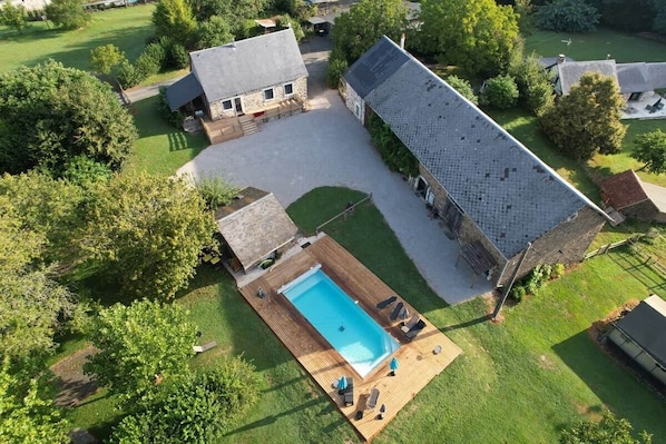 An aerial view of a property with a swimming pool, a covered patio, and a large building with a sloped roof.