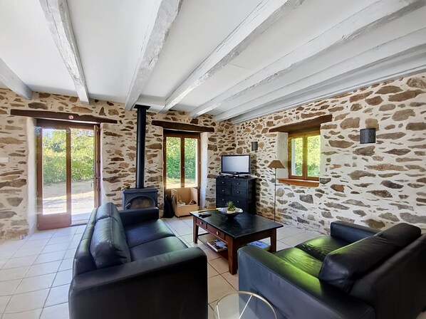 Una sala de estar con paredes de piedra, chimenea, televisor y sofás de cuero.