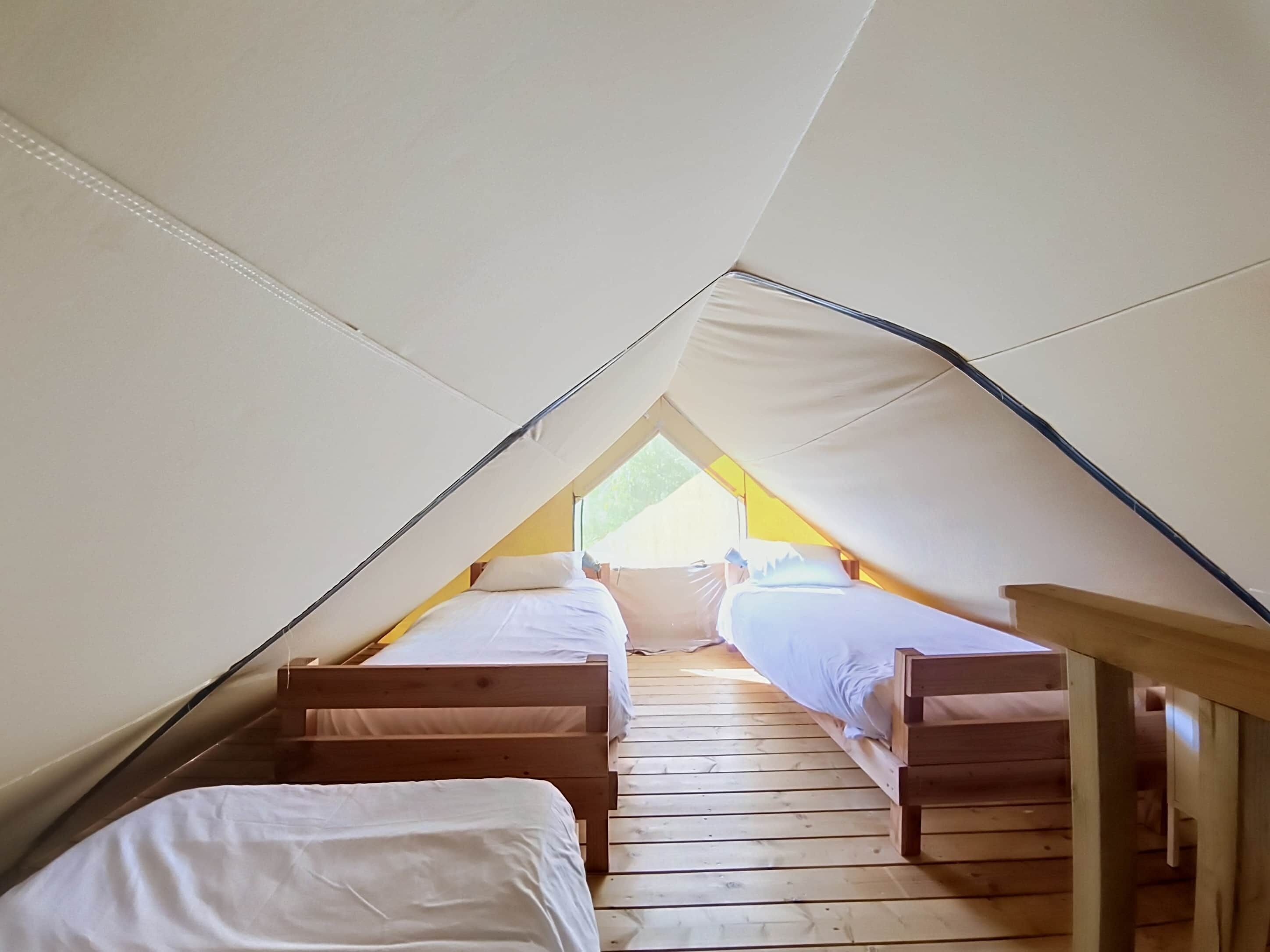 A triangular attic bedroom with two wooden beds and a skylight.
