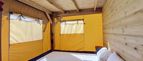 A room with a bed, wooden walls, and a window with a curtain.