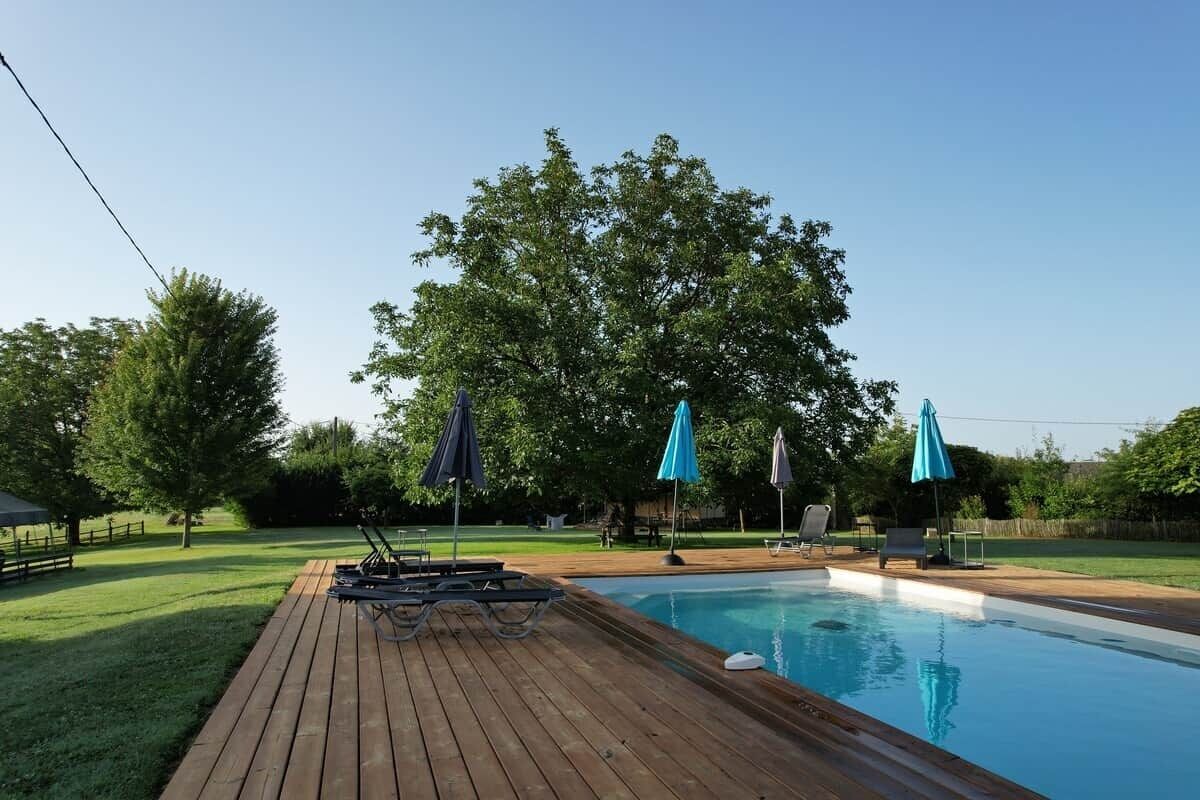 Una piscina con cubierta de madera, sillas de descanso y sombrillas.