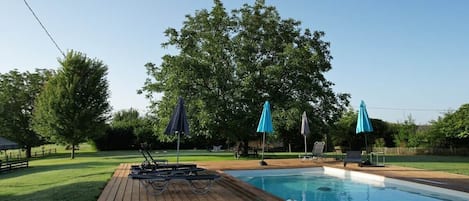 A swimming pool with a wooden deck, lounge chairs, and umbrellas.
