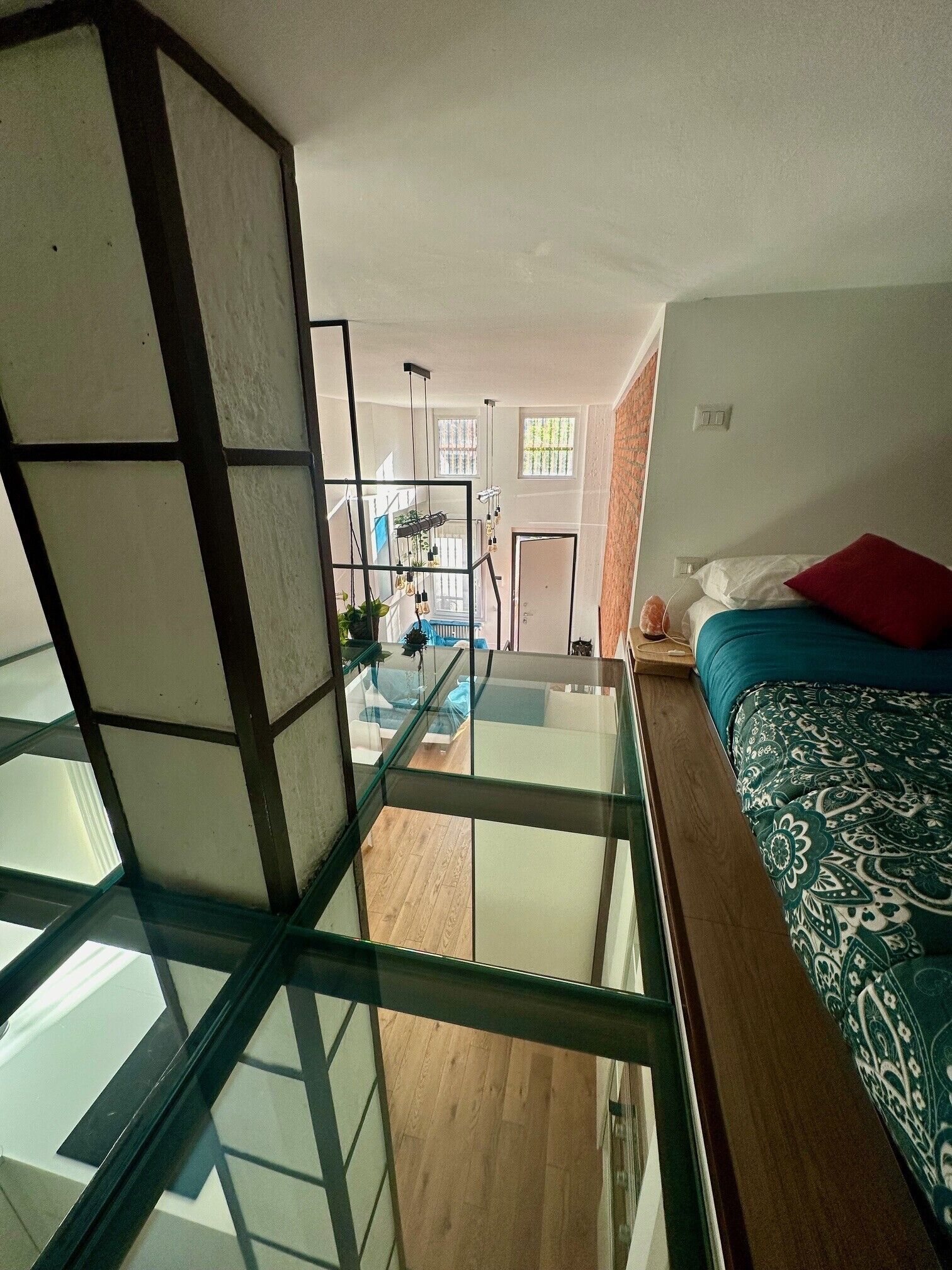 Una habitación con separador de vidrio, una cama con ropa de cama estampada, suelo de madera y vistas al exterior.