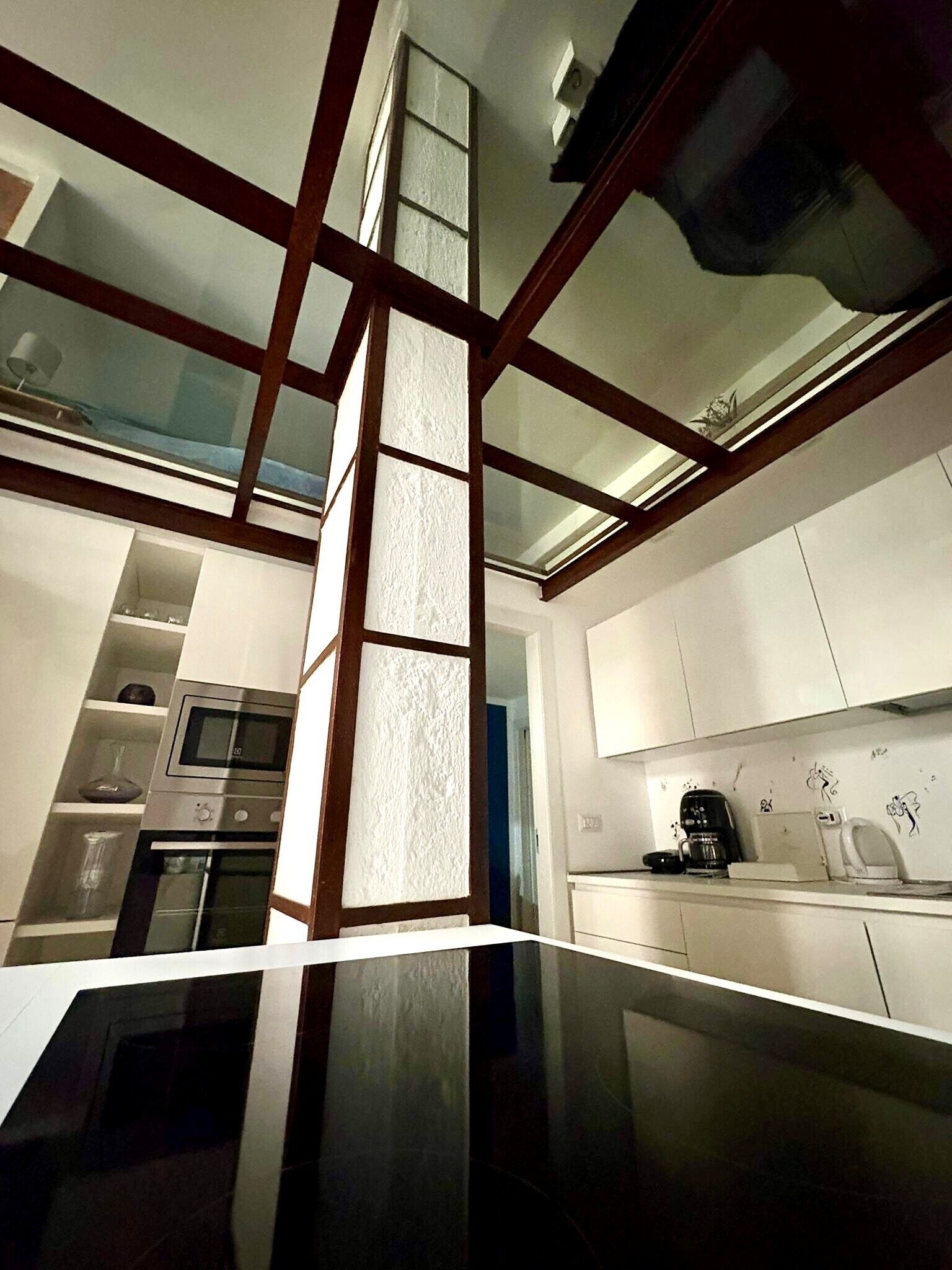 A modern kitchen with a glass partition, stainless steel appliances, and a coffee maker.