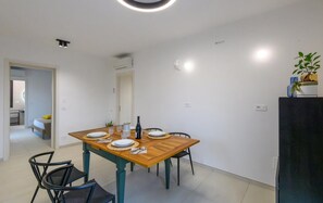 Un coin repas avec une table en bois dressée pour quatre personnes, des chaises et un réfrigérateur sur lequel est posée une plante.
