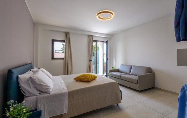 Une chambre d’hôtel moderne équipée d’un lit, d’un canapé, d’une fenêtre et d’une porte donnant sur un espace extérieur.