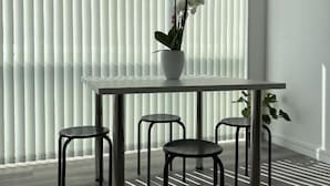 Un comedor con una mesa y cuatro sillas, una planta en maceta y persianas verticales en la ventana.