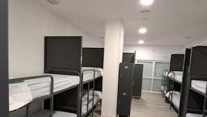 Una habitación con literas, un pilar blanco y una puerta en el centro.