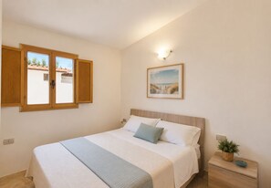A bedroom with a bed, a nightstand, a wall-mounted light, and a window with wooden shutters.