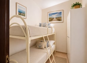 A bunk bed room with a door, a refrigerator, and two framed pictures on the wall.