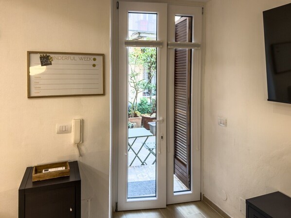 Une pièce avec une porte donnant sur un espace extérieur, un calendrier encadré accroché au mur, une table de chevet avec un plateau, et un téléphone fixé au mur.