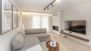 A modern living room with a sofa, a coffee table, a flat-screen TV, and framed artwork on the wall. - Chic Athenian Riviera Retreat in Vari  (Vari)
