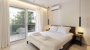 A modern bedroom with a large bed, a nightstand, a bedside table, and a view through a sliding glass door to an outdoor balcony. - Chic Athenian Riviera Retreat in Vari  (Vari)