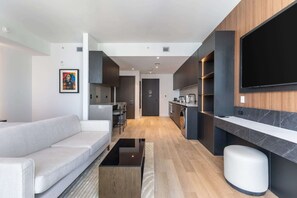 A modern living room with a sofa, a flat-screen TV mounted on the wall, and a kitchen area with a dining set. - E11even Serenity Rooftop Pool (Miami)