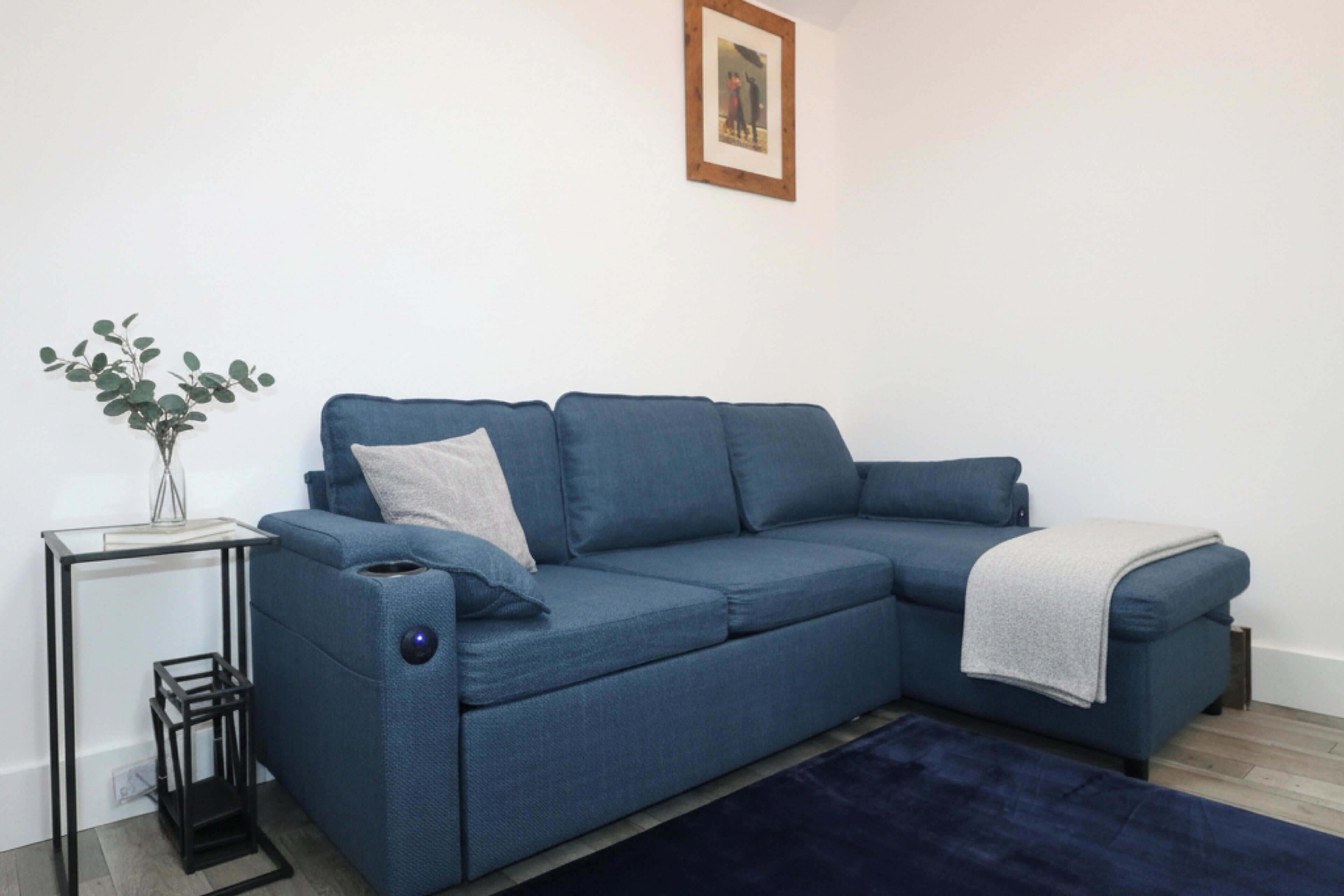 A blue sectional sofa with a side table and a vase of green leaves.