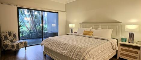 A bedroom with a large bed, two bedside tables, a chair, and a sliding glass door leading to a balcony.