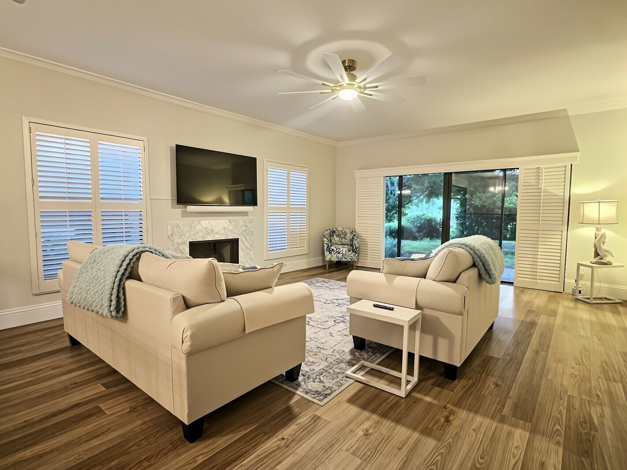 A living room with two sofas, a fireplace, a flat-screen TV, and a ceiling fan.
