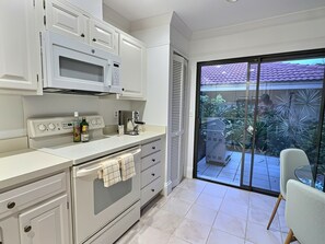 Eine moderne Küche mit integriertem Mikrowellenherd, Backofen und Kaffeemaschine. Eine Schiebetür führt auf einen Balkon mit Blick ins Freie.