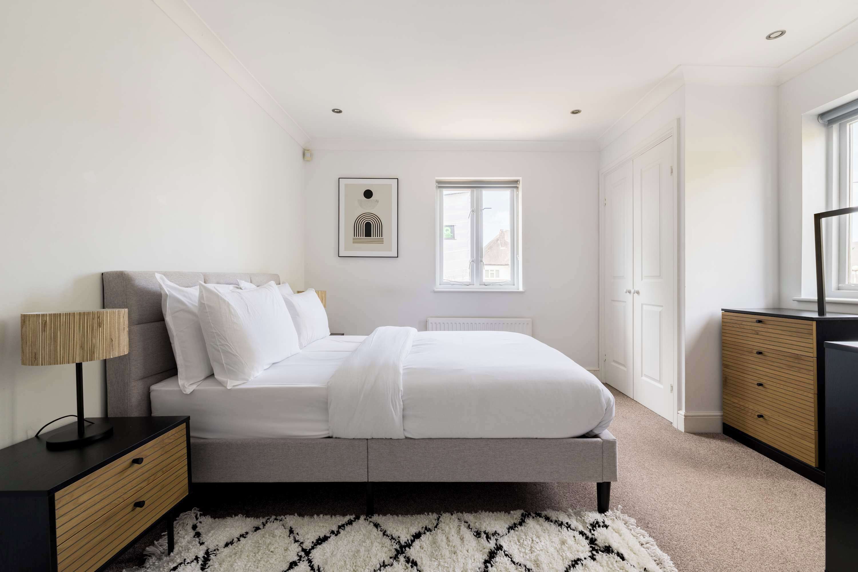 Une chambre à coucher avec un lit, une table de chevet, une lampe, une commode et un tableau encadré au mur.