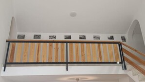 A staircase with a wooden handrail and a black metal railing, leading to a landing with a white wall and a series of black-and-white photographs.